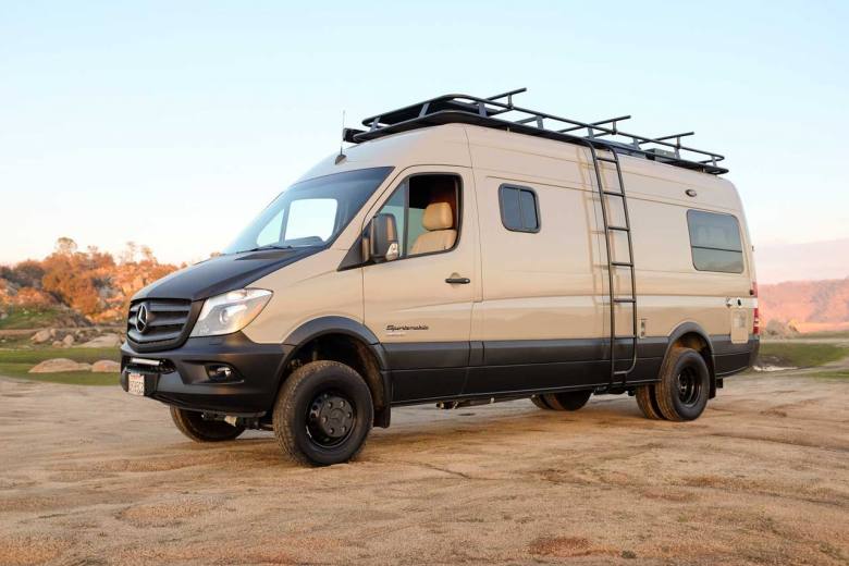 A custom Sportsmobile Sprinter 4x4 conversion featuring a Thule roof rack, side ladder, and rocker panel coating on the sands of the Mojave desert.