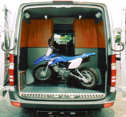 Rear view of a motorcycle parked in the cargo area of a white Sportsmobile conversions van.