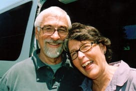 Jim and Karen Duncan smiling and laughing next to their white Sportsmobile custom camper van.